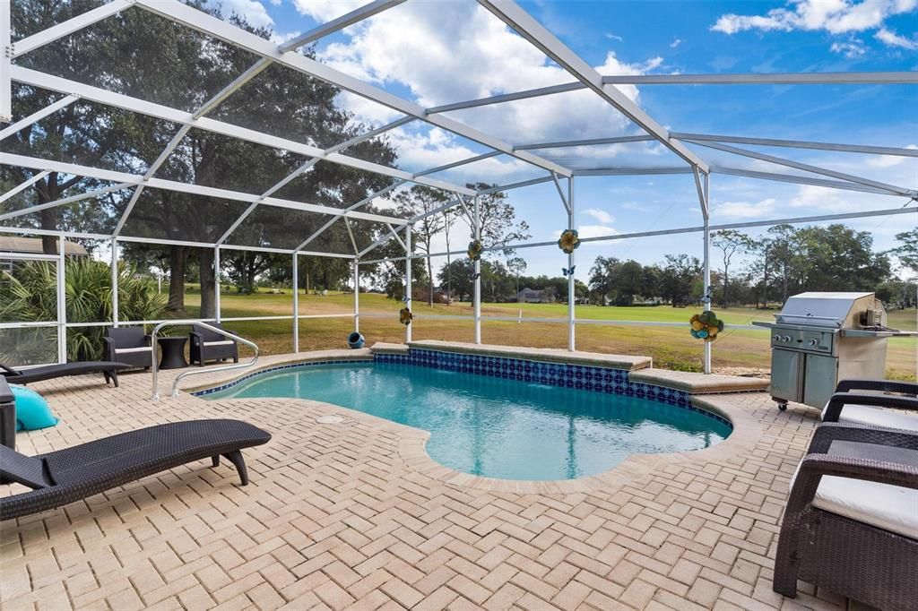 Screened enclosed swimming pool features brick paver patio and views of golf course.