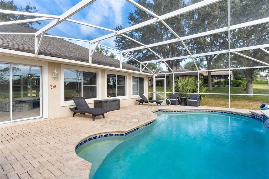 Screened enclosed swimming pool features brick paver patio and views of golf course.