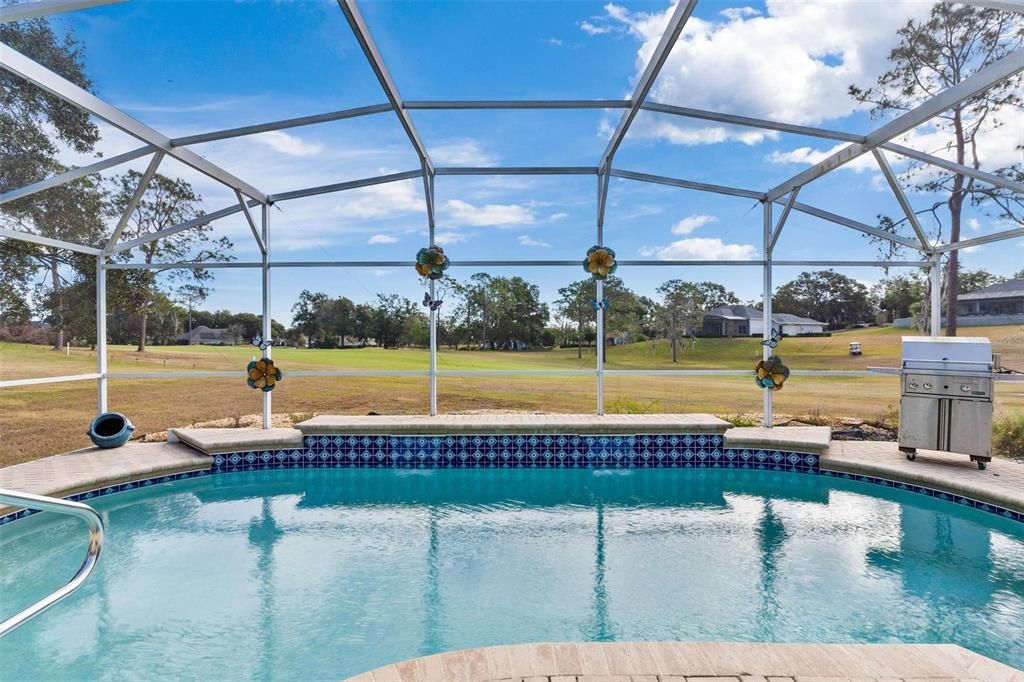 Screened enclosed swimming pool features brick paver patio and views of golf course.