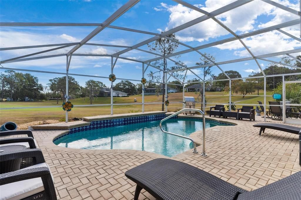 Screened enclosed swimming pool features brick paver patio and views of golf course.