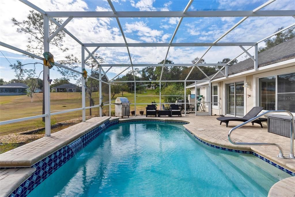 Screened enclosed swimming pool features brick paver patio and views of golf course.