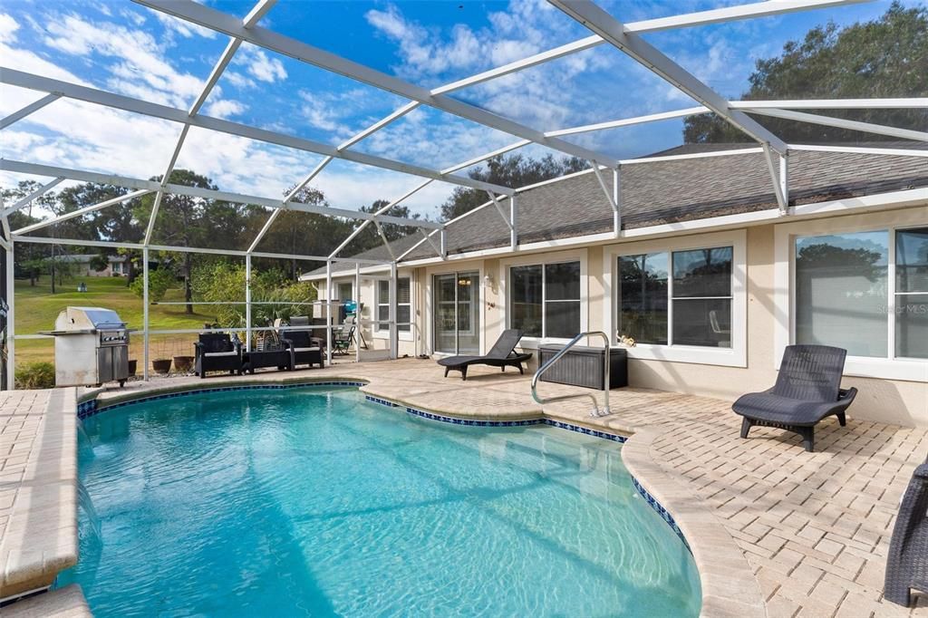 Screened enclosed swimming pool features brick paver patio and views of golf course.