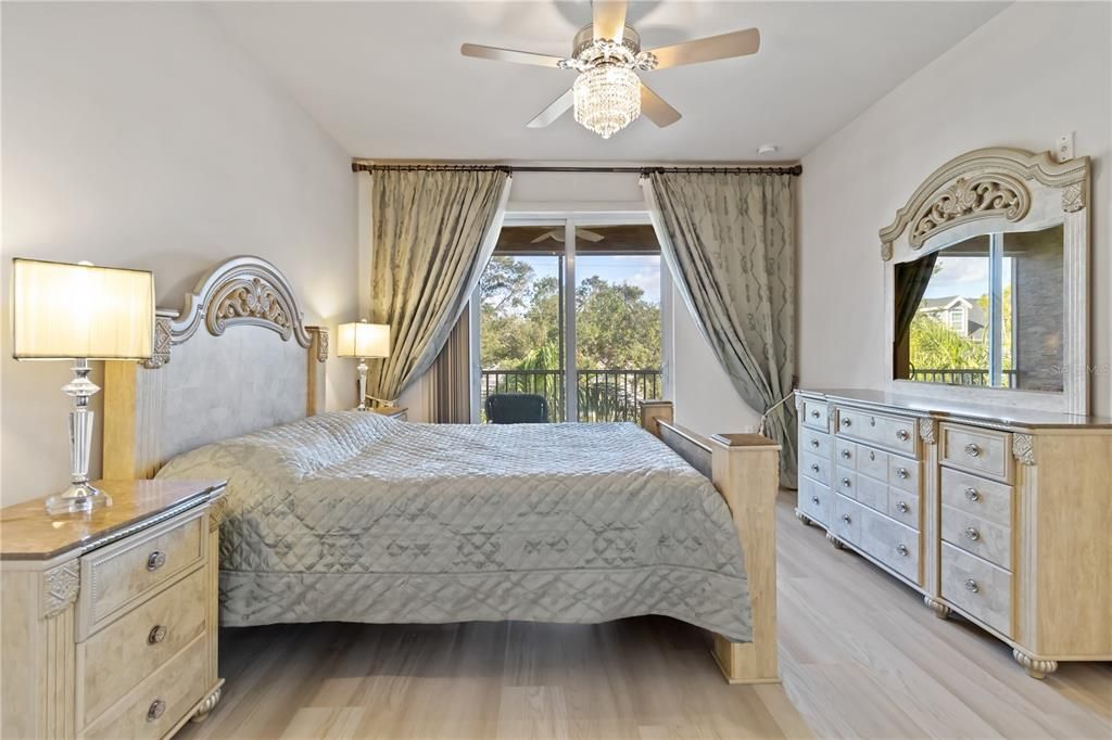 Primary bedroom with private entrance to balcony, fan with chandelier and luxury vinyl flooring.