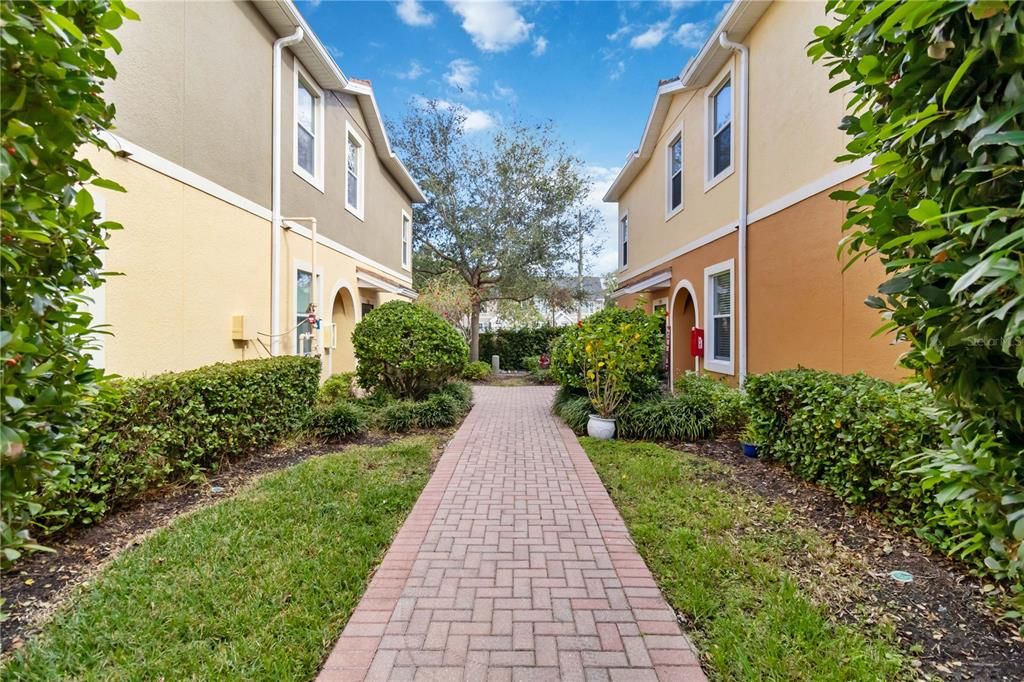 Brick paved pathway around building leading to on of the two private entrances to home