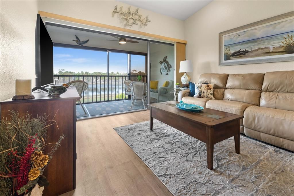 THE LIVING ROOM HAS VAULTED CELINGS AND SLIDING DOORS THAT ACCESS AN ENCLOSED LANAI