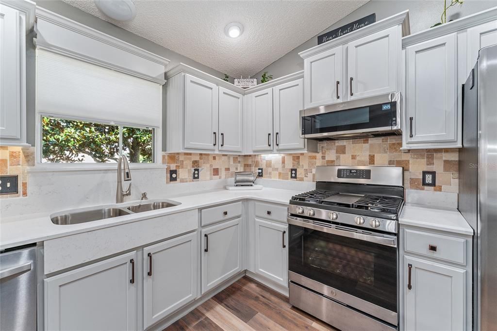 KITCHEN - Note these extras: Wooden CORNICE over window, undermount DOUBLE BOWL SINK with PULL DOWN FAUCET and additional QUARTZ PANEL on top front of under sink cabinets, updated hardware, and sleek SS APPLIANCES.