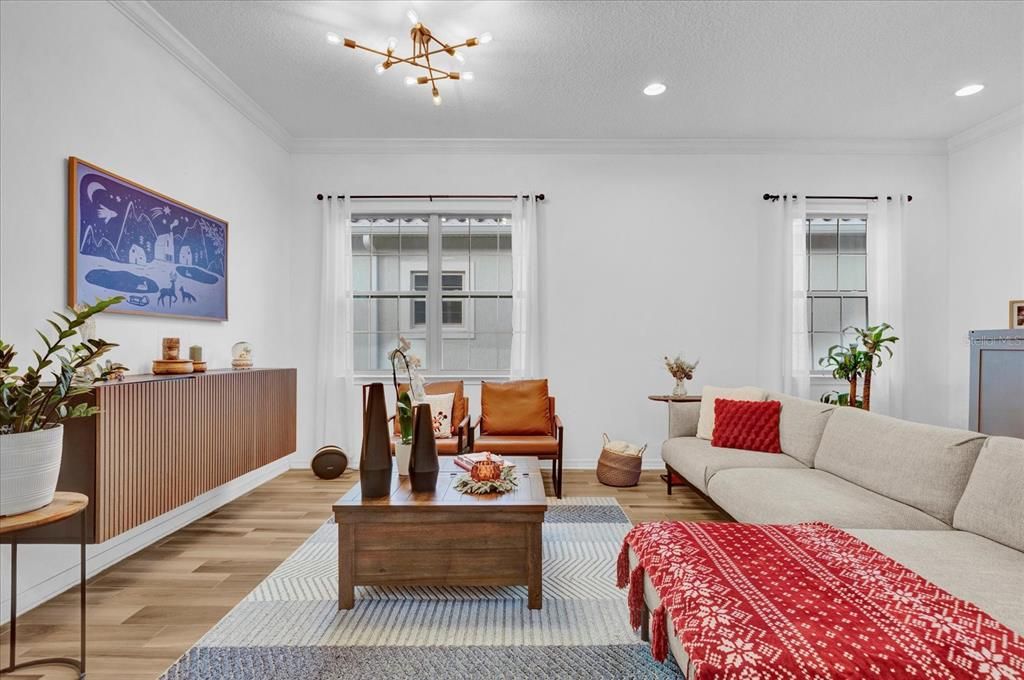 Step into this bright and inviting living room, featuring elegant wood-look tile flooring, large windows that let in ample natural light, and a modern light fixture that adds a touch of sophistication. The open layout offers a perfect blend of comfort and style, making it ideal for entertaining or relaxing with family.