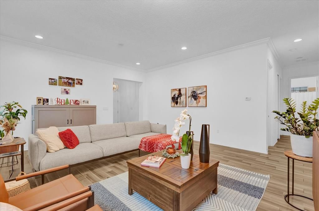 Step into this bright and inviting living room, featuring elegant wood-look tile flooring, large windows that let in ample natural light, and a modern light fixture that adds a touch of sophistication. The open layout offers a perfect blend of comfort and style, making it ideal for entertaining or relaxing with family.