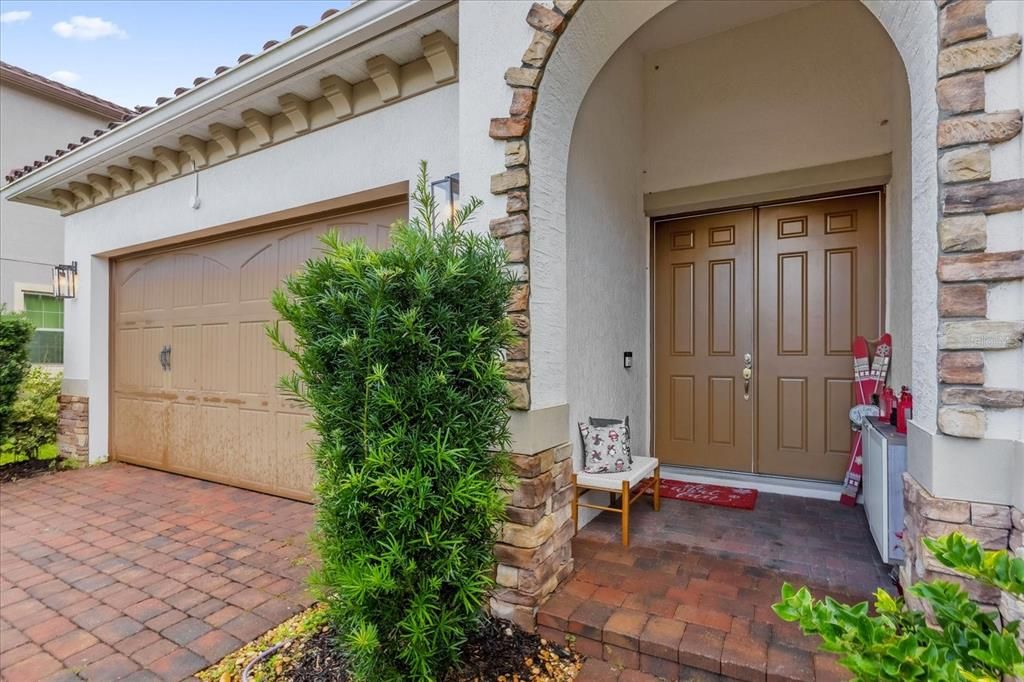 A beautiful Mediterranean-style home featuring elegant clay roof tiles, a stylish arched entryway, and a paved driveway. The landscaping completes this stunning curb appeal in the Eagle Creek Community of Lake Nona.