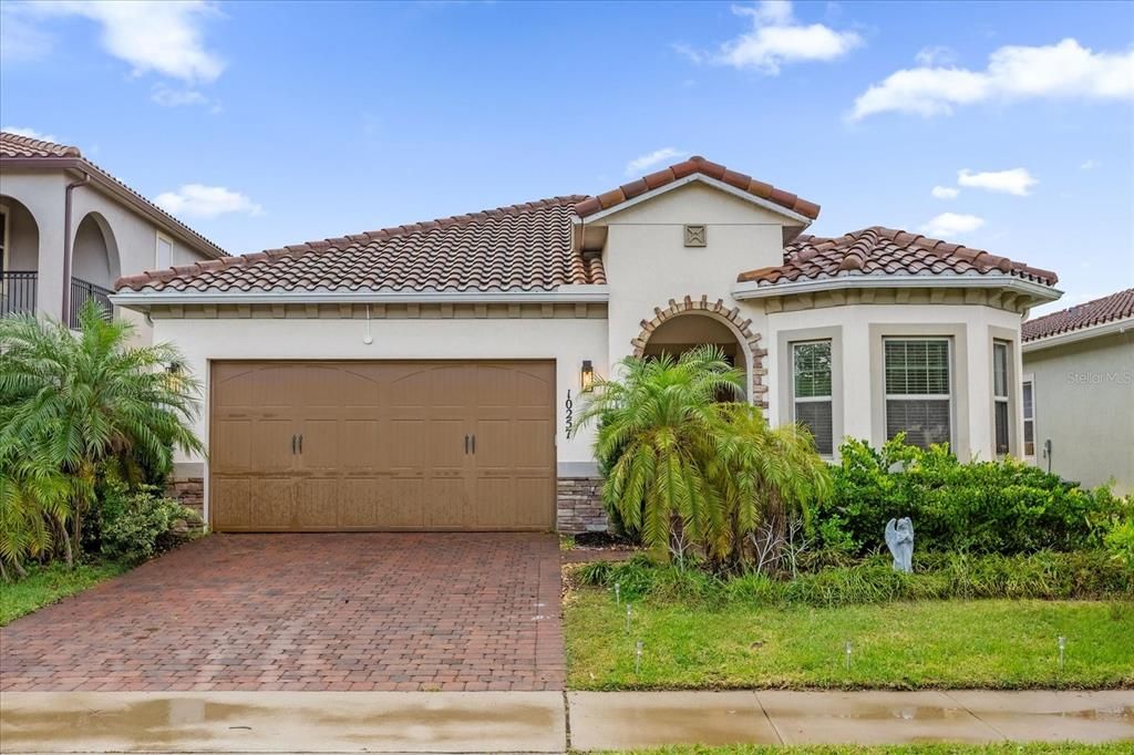 A beautiful Mediterranean-style home featuring elegant clay roof tiles, a stylish arched entryway, and a paved driveway. The landscaping completes this stunning curb appeal in the Eagle Creek Community of Lake Nona.