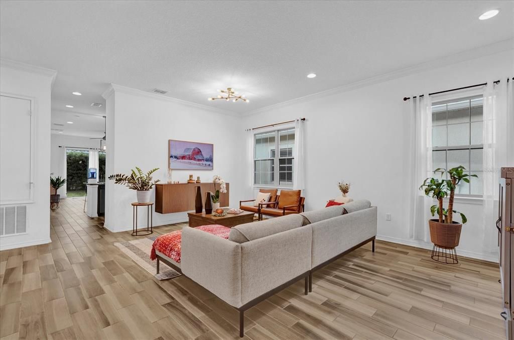 Step into this bright and inviting living room, featuring elegant wood-look tile flooring, large windows that let in ample natural light, and a modern light fixture that adds a touch of sophistication. The open layout offers a perfect blend of comfort and style, making it ideal for entertaining or relaxing with family.