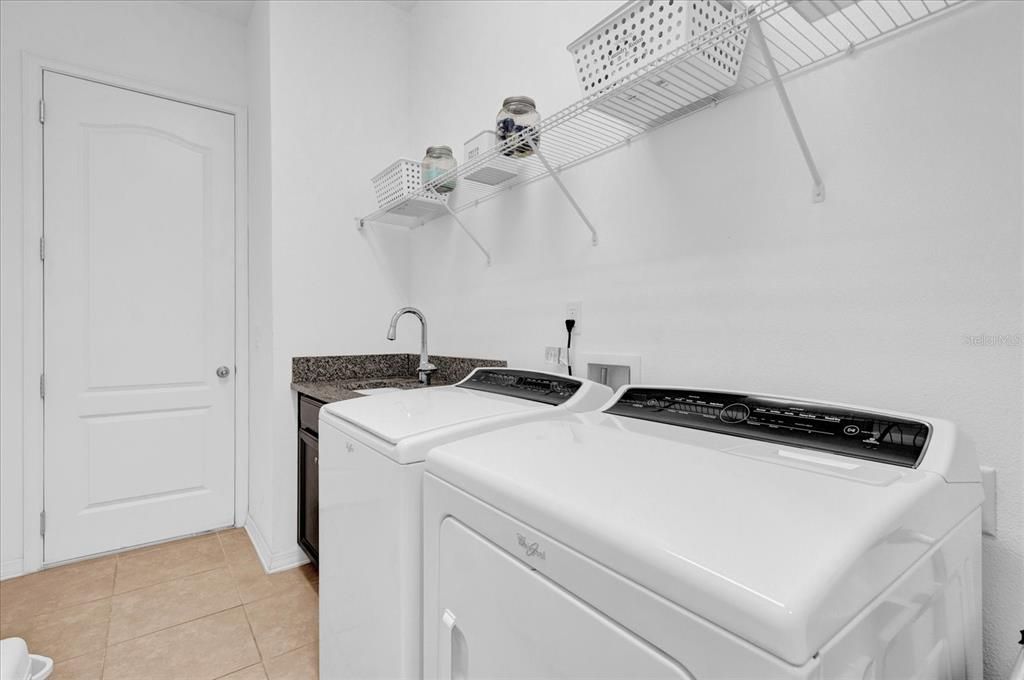 This laundry room combines functionality and style, featuring a built-in sink for added convenience. Open shelving provides ample storage for organization, while the modern washer and dryer make laundry tasks a breeze.