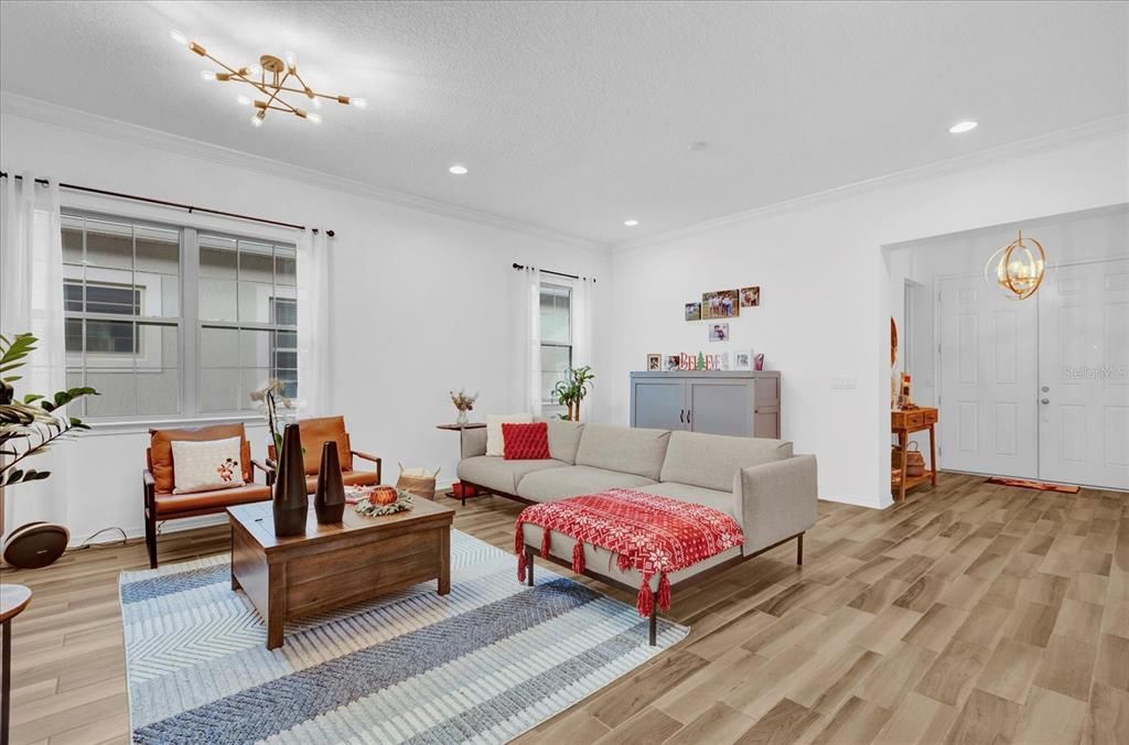 Step into this bright and inviting living room, featuring elegant wood-look tile flooring, large windows that let in ample natural light, and a modern light fixture that adds a touch of sophistication. The open layout offers a perfect blend of comfort and style, making it ideal for entertaining or relaxing with family.