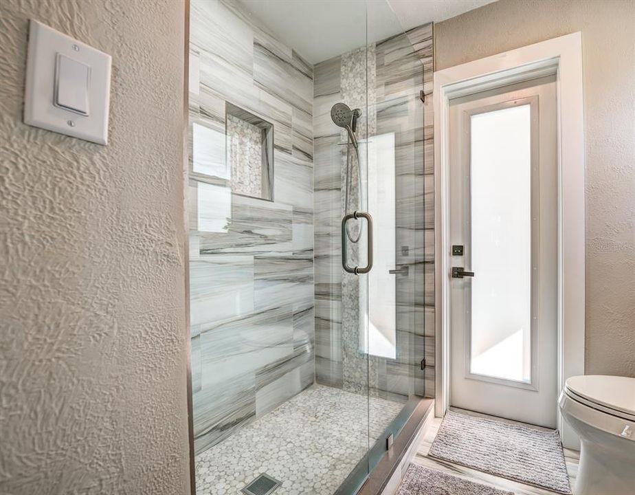 Stunning porcelain tiled floors and shower walls grace the updated primary bath. A shampoo niche, frameless glass shower enclosure and a built in shower bench were added. New plumbing fixtures and commodes were installed in both bathrooms.