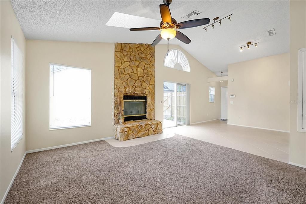 Living room with stone fireplace, ceiling fan, vaulted ceilings and skylights