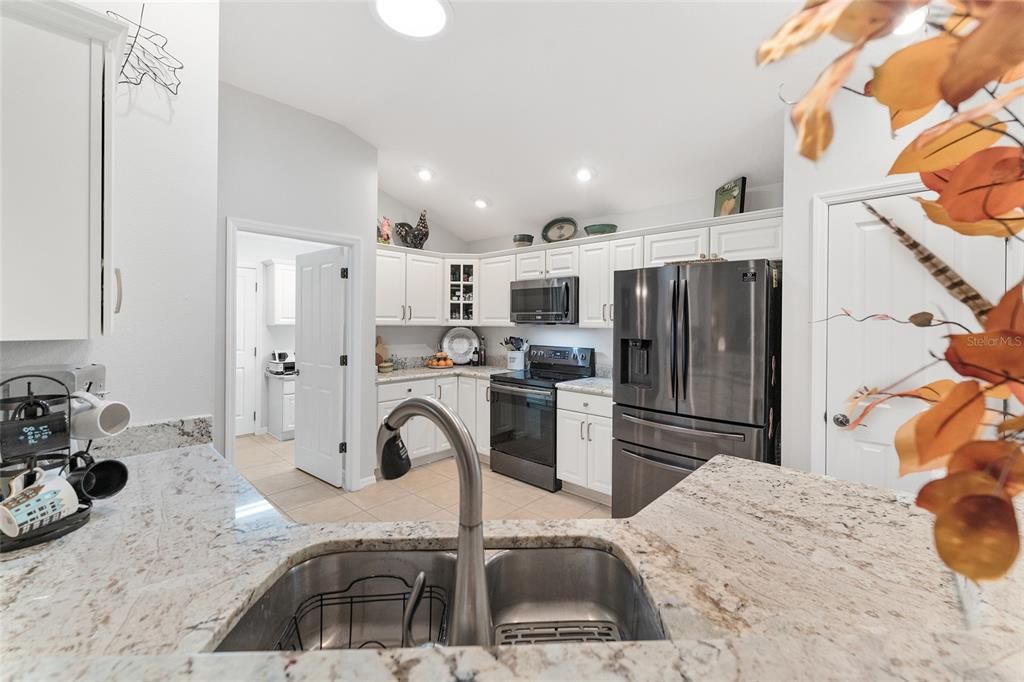 View of KITCHEN over BREAKFAST BAR - Shows beautiful GRANITE COUNTERTOPS with undermount sink & pull down faucet, timeless WHITE CABINETS w/ crown molding, PULL OUTS, LAZY SUSAN, SS APPLIANCES, and SOLAR TUBE for NATURAL LIGHT.