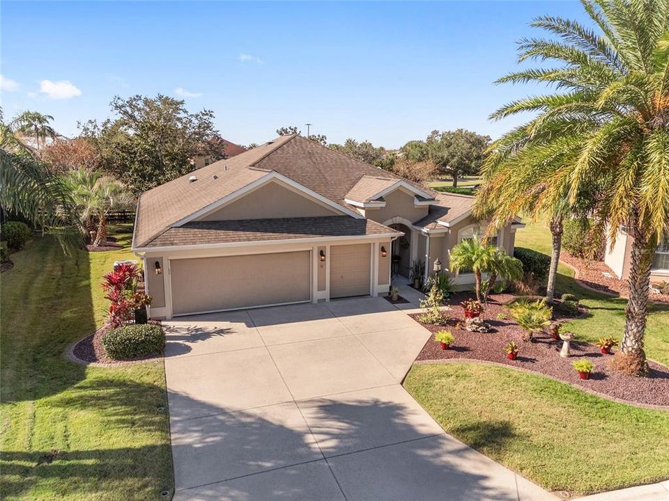 FRONT EXTERIOR - Low aerial view shows MATURE LANDSCAPING w/ concrete curbing, rock filled beds and several varieties of PALM TREES.