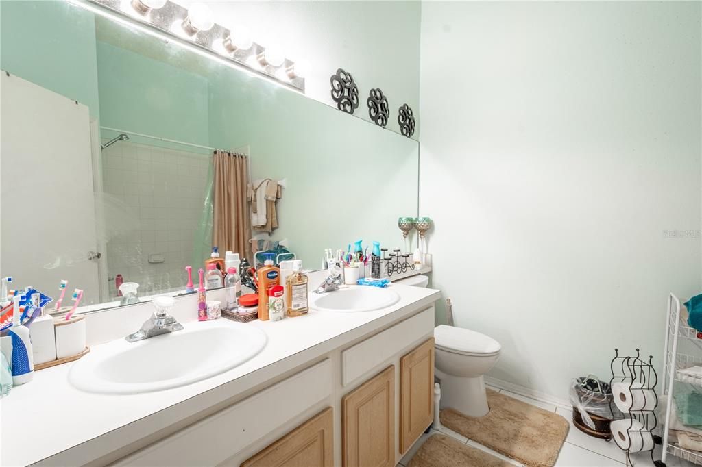 2nd floor bathroom features a mirrored vanity with dual sinks and storage, ceramic tile floor and a tub with shower.