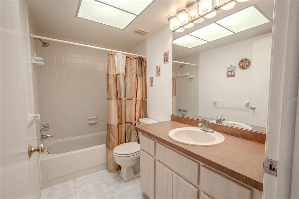 The 2nd bathroom features a tub with shower and a mirrored vanity with torage and down light fixture.