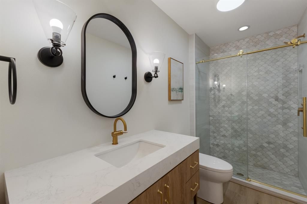 Bathroom #2 w/ porcelain tiled shower and single vanity w/ quartz counters and gold hardware