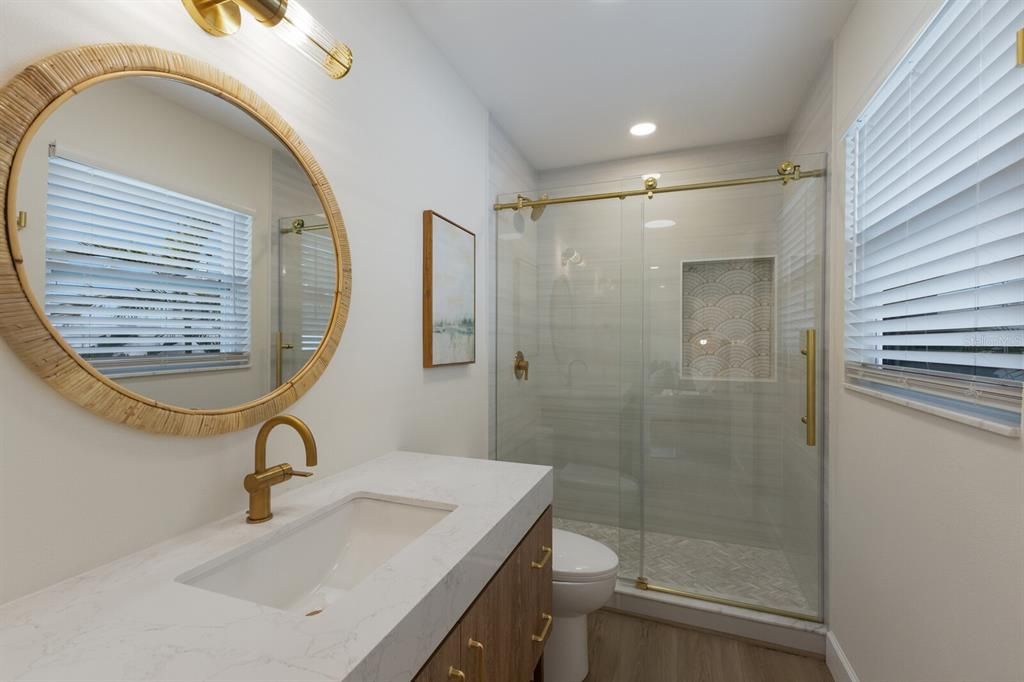 Primary  en suite bathroom w/ glassed-in porcelain tiled shower and quartz counter top vanity