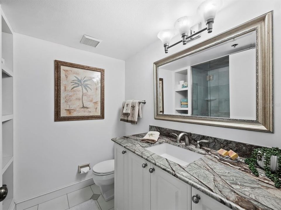 The guest bathroom is adorned with a large beautifully framed mirror, spacious vanity with granite countertops, and built-in shelving for towels and linens.