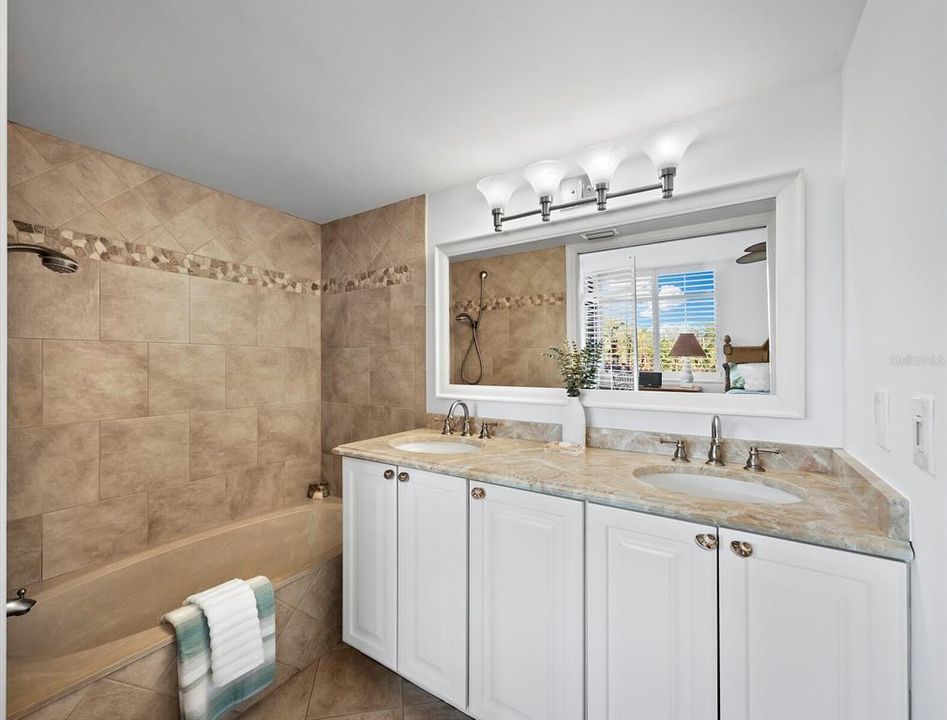 This ensuite bath features elegant tile flooring and granite countertops, with a dual sink vanity offering ample storage for convenience. The space includes a bathtub with a showerhead, creating a perfect blend of relaxation and functionality.