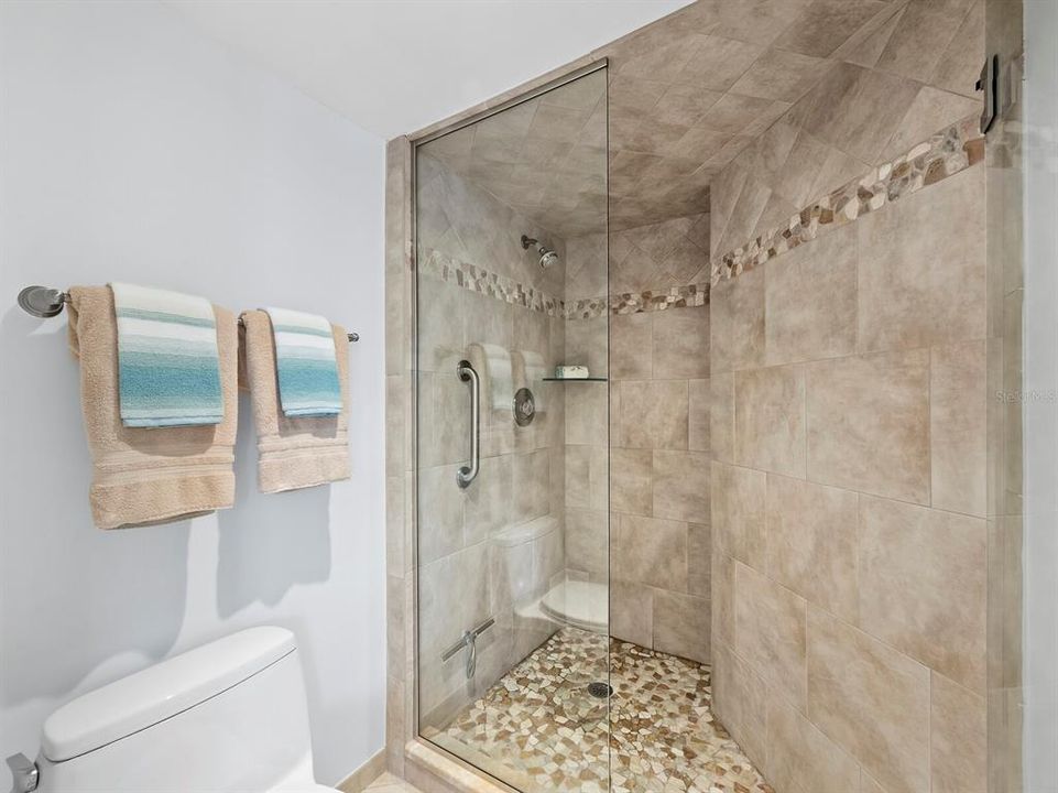 This ensuite includes a separate lavatory for added privacy, along with a sleek glass shower stall featuring floor-to-ceiling tile and a mosaic border, creating a modern and stylish touch.