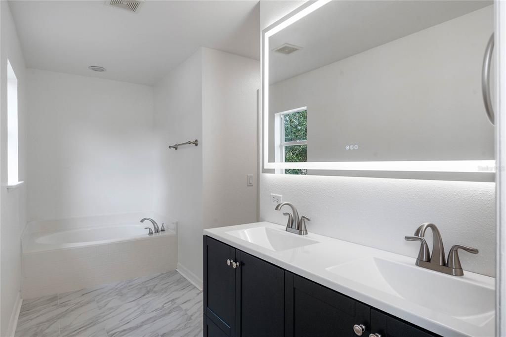 Primary bathroom with dual sinks, large soaking tub and lighted mirror.