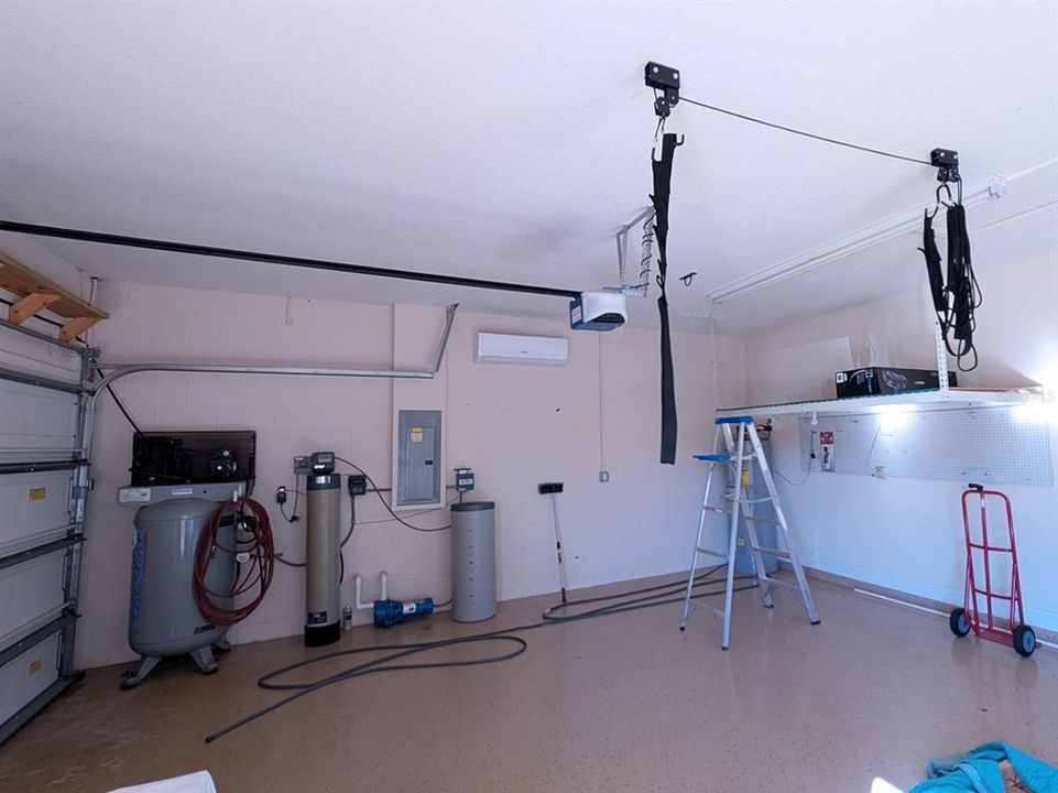 3 car garage has epoxy floor treatment and conveys with industrial air compressor, ceiling mounted storage rack, pulley system storage and peg boards