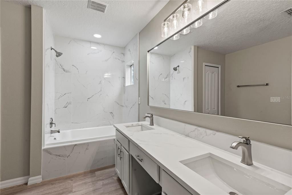 Master Bath features new LVP flooring, double quartz topped vanity, tile shower tub/combo and walk in closet