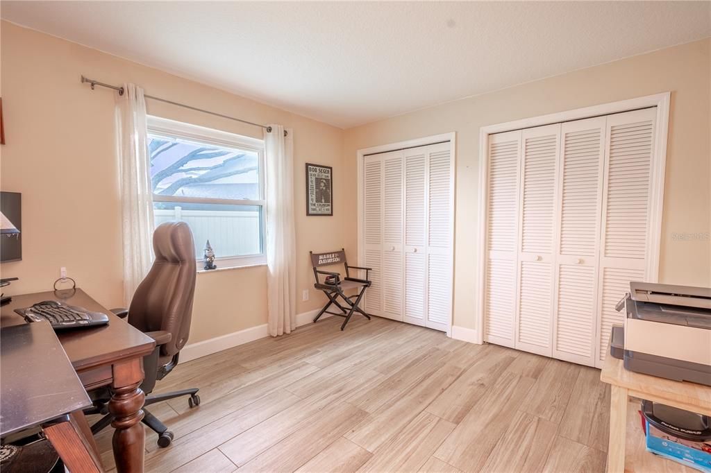 Bedroom 3, currently used as a home office, features wood-look porcelain tile and dual built in closets with shutter doors.