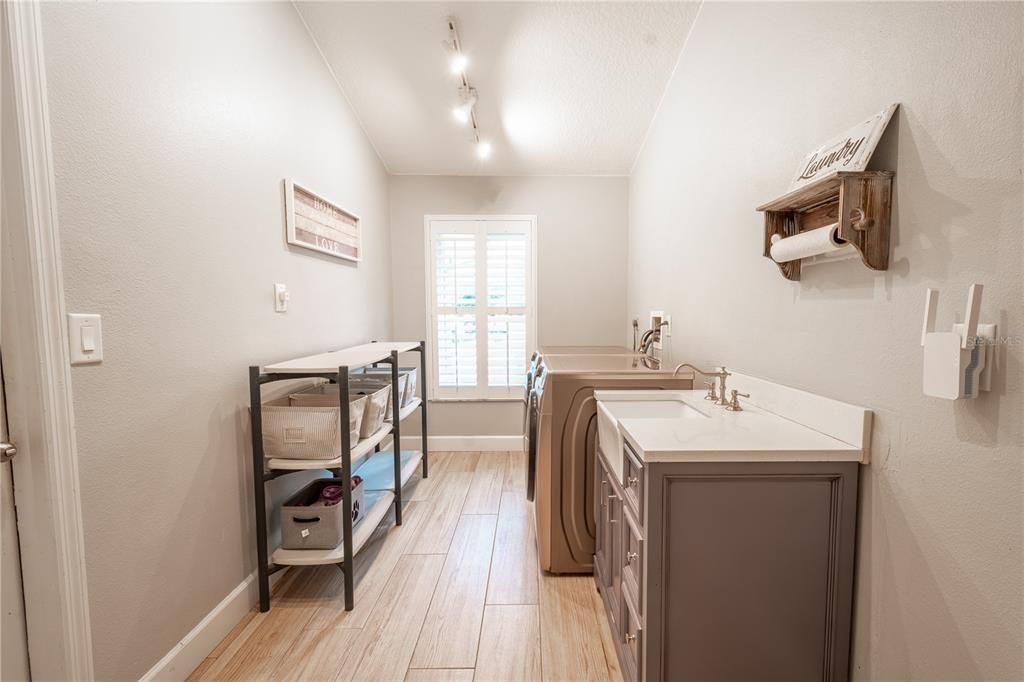 The laundry room is spacious, with a vaulted ceiling, stylish porcelain farm sink and cabinet with storage, porcelain tile flooring and washer/dryer hook-ups.