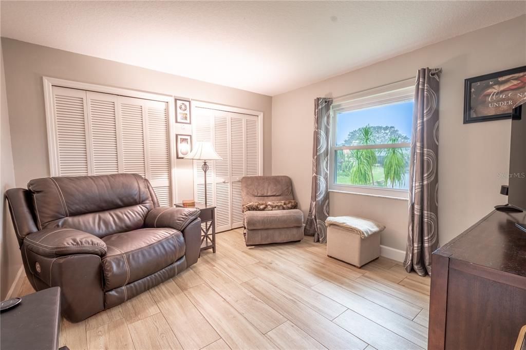 Bedroom 2, currently used as a den, features wood-look porcelain tile and dual built in closets with shutter doors.