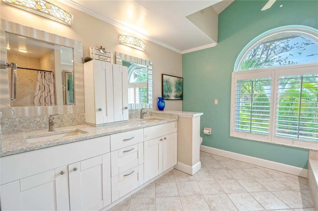 The primary bathroom features a mirrored, solid wood, dual sink vanity with a stone countertop and stylish light fixtures.