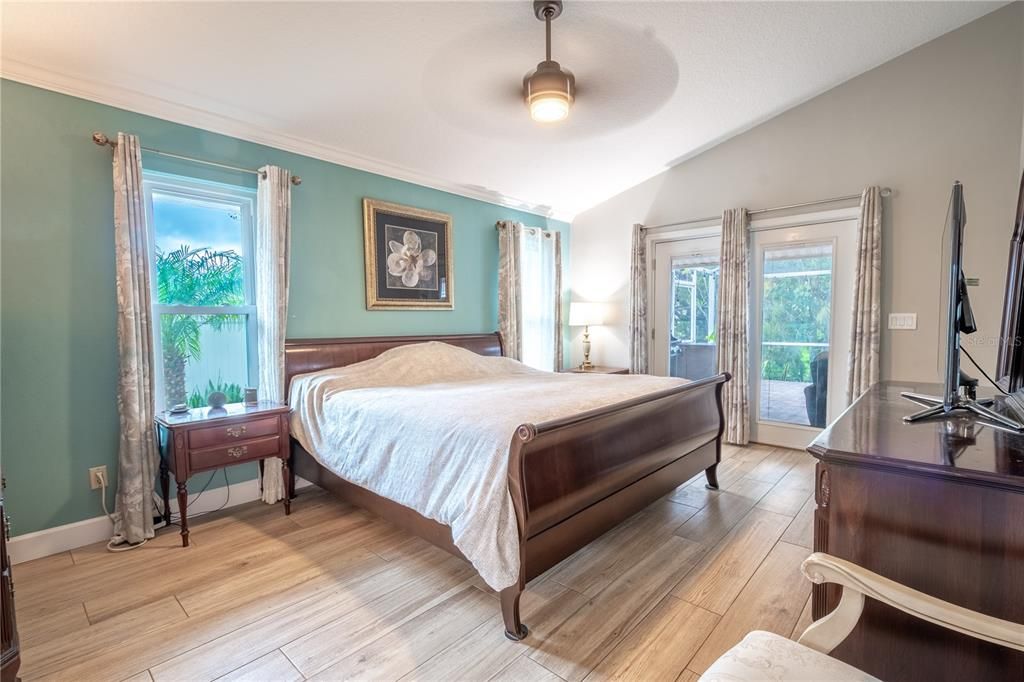 The primary bedroom features a vaulted ceiling with ceiling fan, wood-look porcelain tile floor and french doors to the lanai.