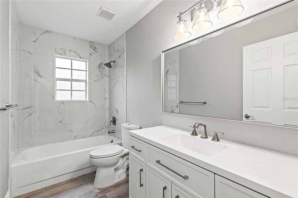 Redesigned hallway bath features a granite top vanity and marble tile shower/tub combo.