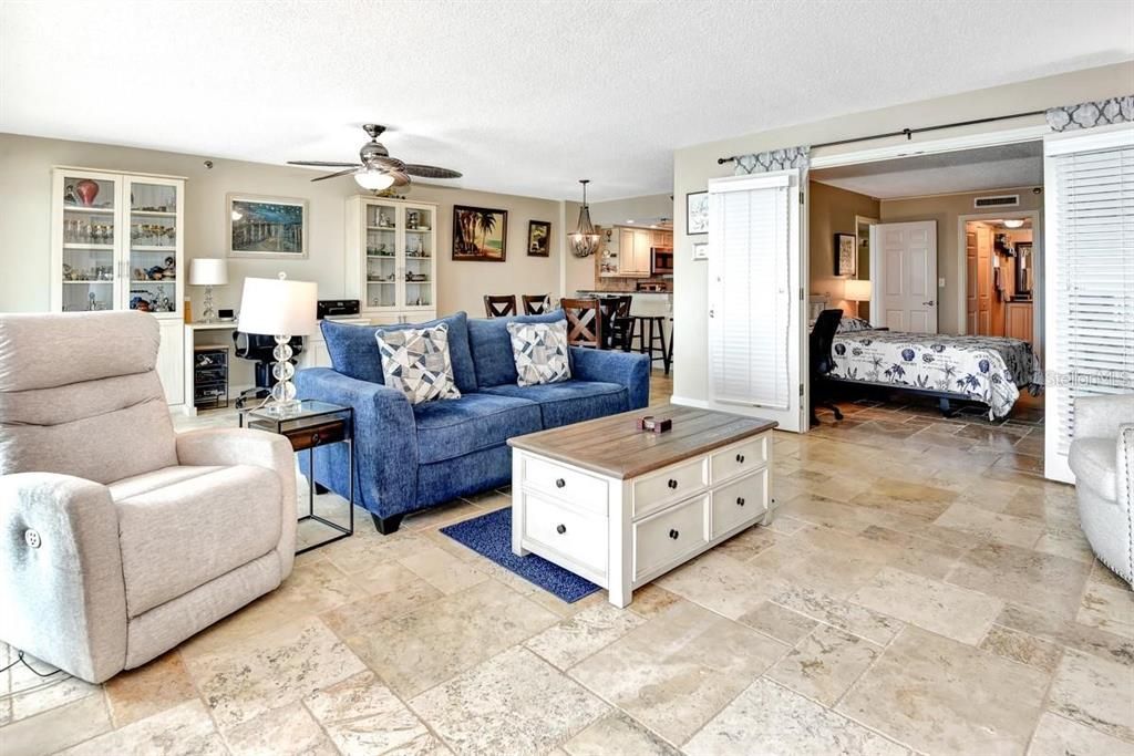 Spacious living room with travertine flooring, a cozy atmosphere, and direct access to the primary suite for seamless functionality.