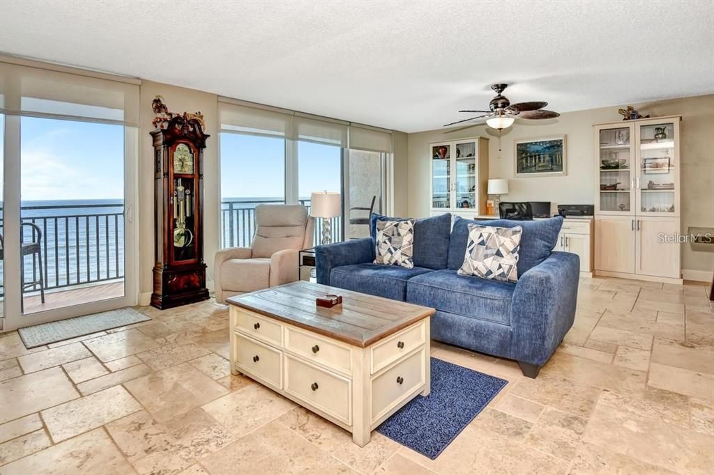 Spacious living room with travertine flooring, a cozy atmosphere, and direct access to the primary suite for seamless functionality.