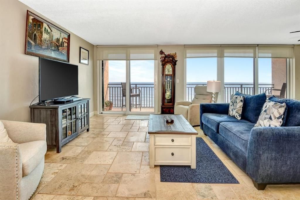 Spacious living room with travertine flooring, a cozy atmosphere, and direct access to the primary suite for seamless functionality.