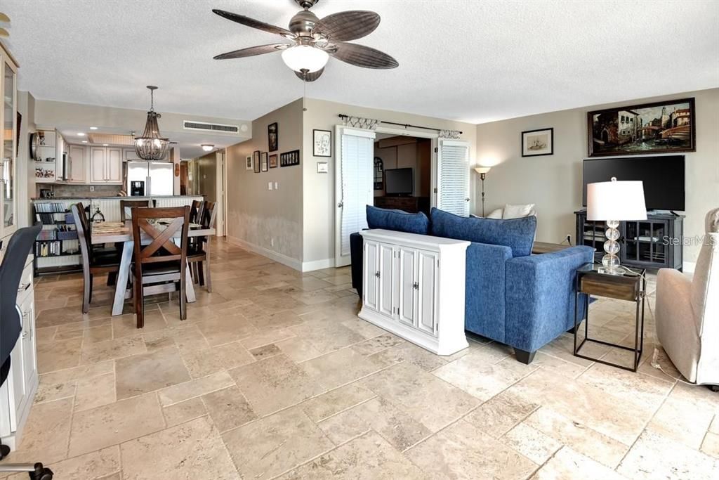 Spacious living room with travertine flooring, a cozy atmosphere, and direct access to the primary suite for seamless functionality.