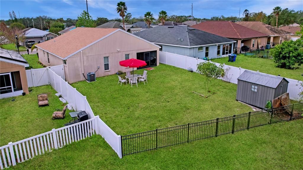 Spacious fenced backyard featuring outdoor seating with a red patio umbrella and a storage shed.