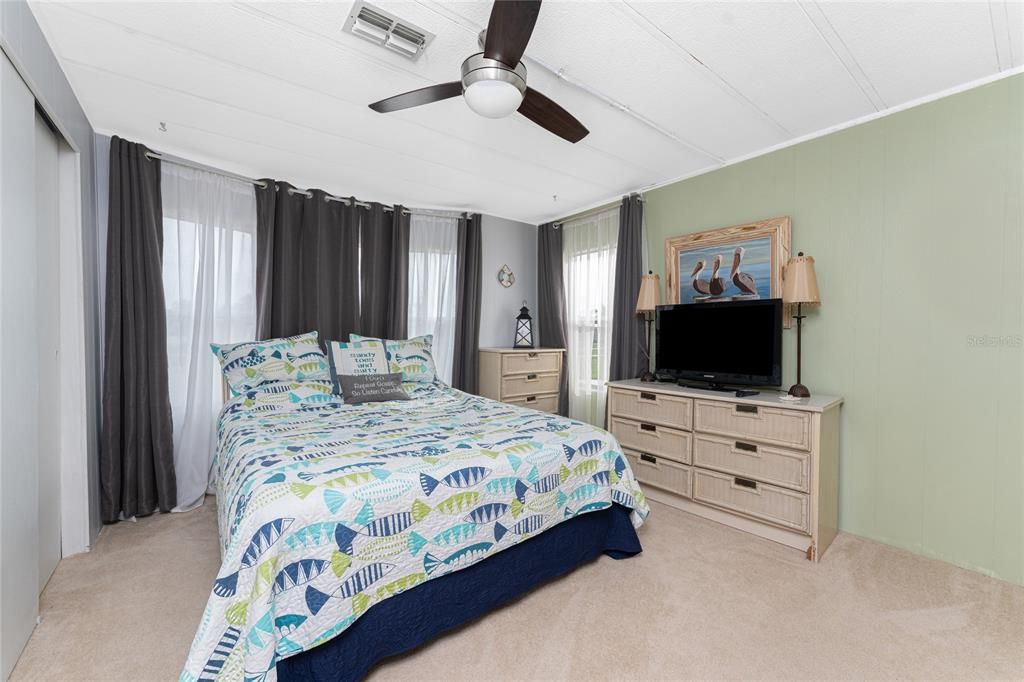 The guest bedroom has a ceiling fan and carpeted flooring.