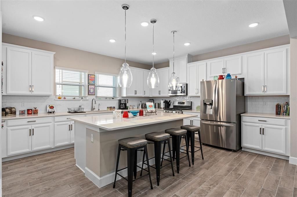 Enjoy this Very Functional Kitchen Offering 42" Solid Wood Cabinetry, Under Cabinet Lighting, Quartz Countertops, Tiled Backsplash, Large Island with Pendent Lighting and a Breakfast Bar, Upgraded Stainless Appliances and a Large Walk-In Pantry. The Microwave is vented to the outside.