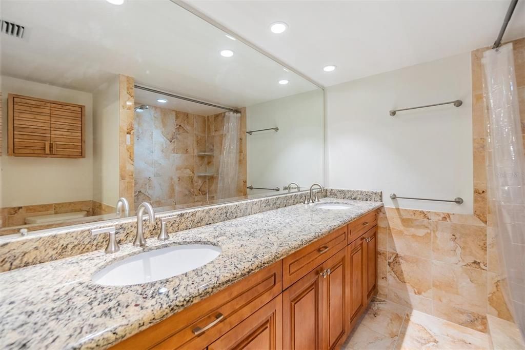 Primary ensuite bathroom with dual sink, granite countertops, wood vanity, walk in shower and stylish granite surround.