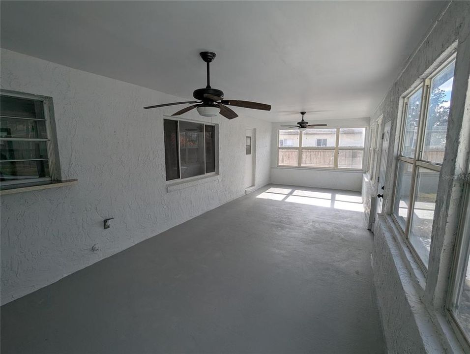 Large rear porch with dual fans and window to dining room, pass-thru window to kitchen and door to primary bathroom