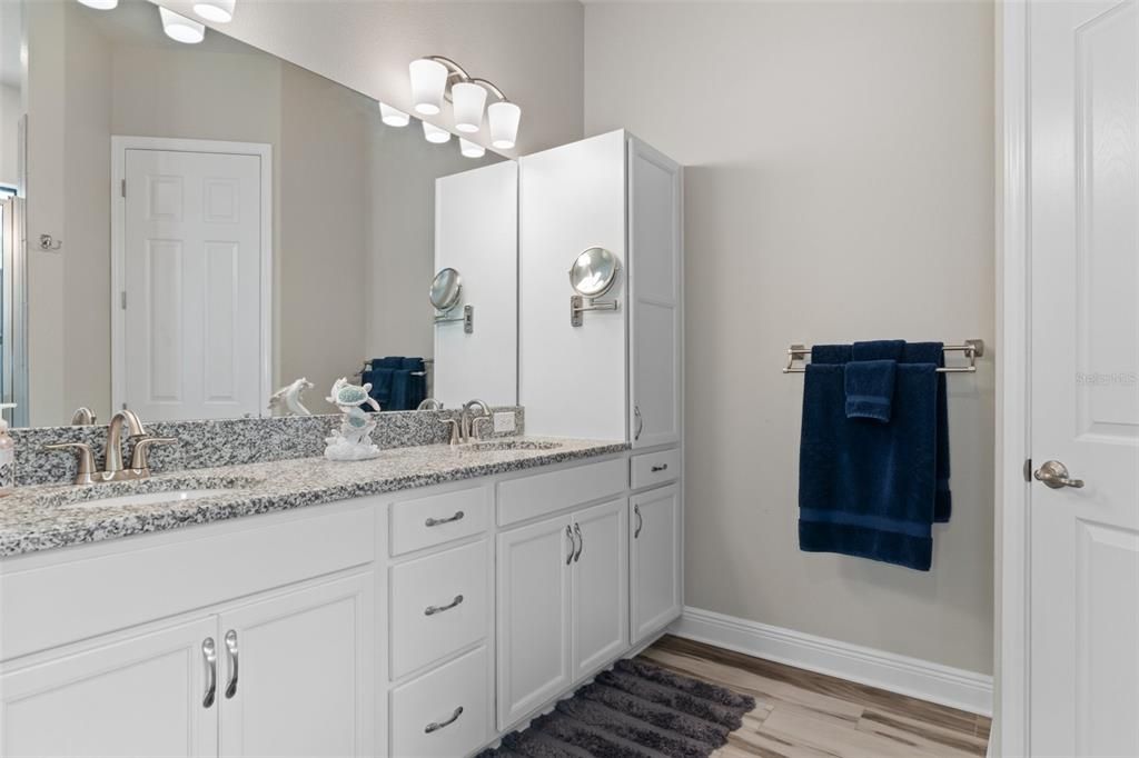 The bath vanity with dual sinks features a spacious granite countertop, ample storage, including a tall storage cabinet. Door on the right is to the private water closet.