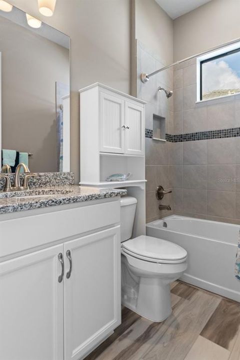 The home decor finishes carry into the guest bath and features a comfort height vanity and commode; as well as contrast tile ribbon in the shower surround and a shampoo niche.