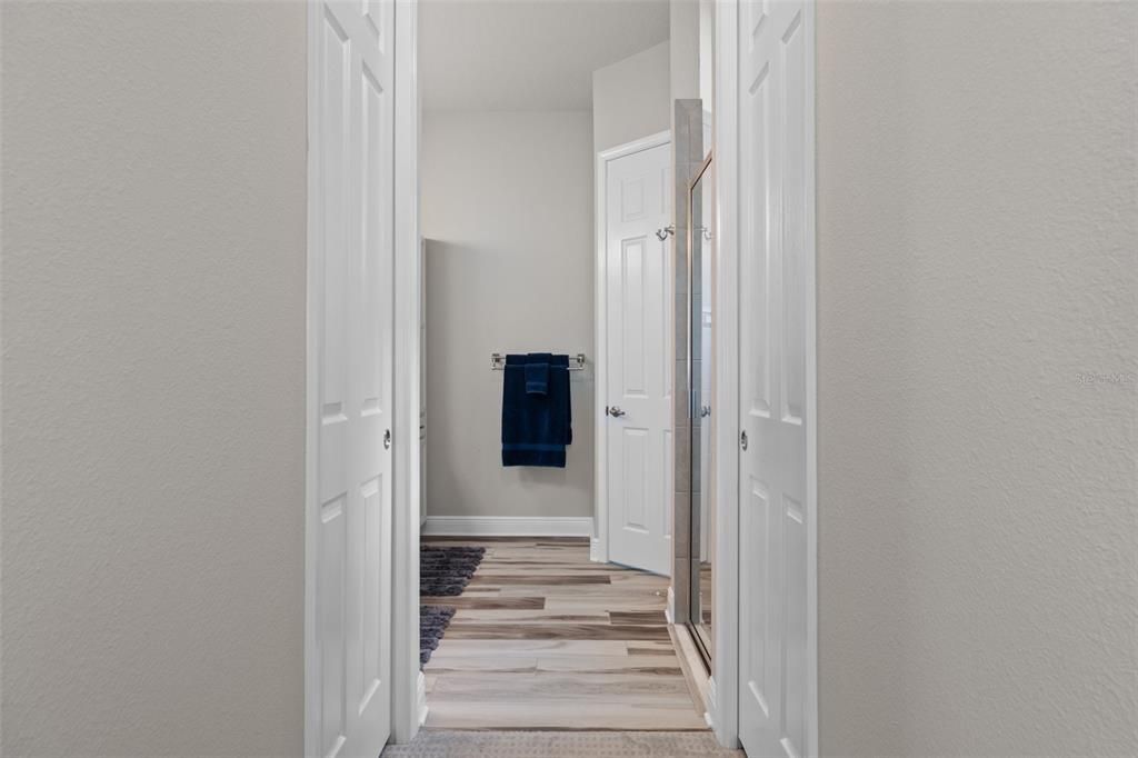 The hallway into the primary bath is flanked by walk-in closets on either side.