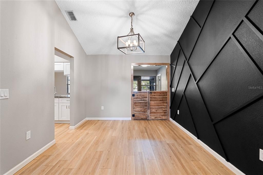 Versatile interior space. The room features sleek light wood flooring and neutral-toned walls, creating a bright and modern feel. A bold accent wall with geometric black paneling adds a touch of drama and sophistication.